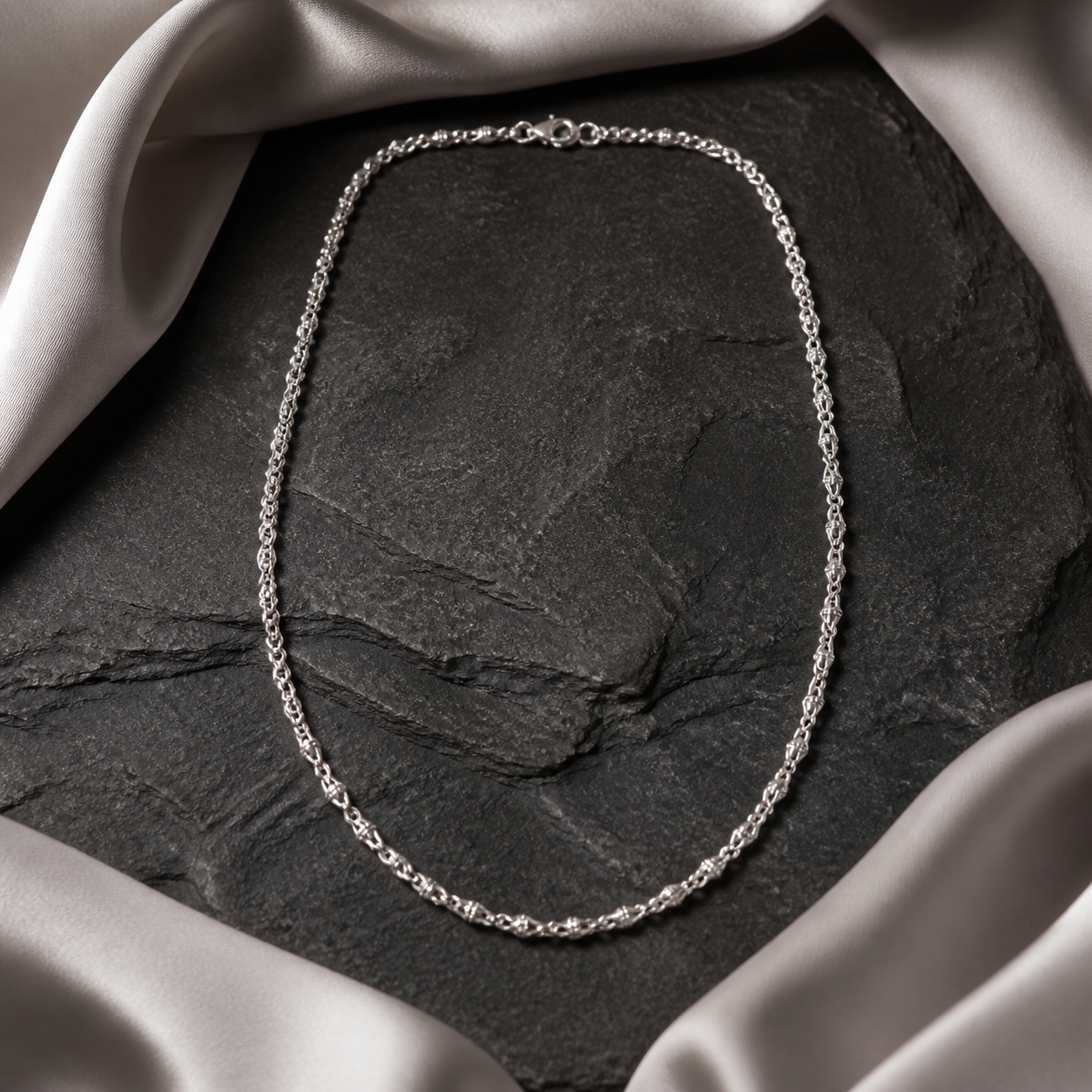Fine silver neck chain arranged on charcoal stone and pearl-grey silk